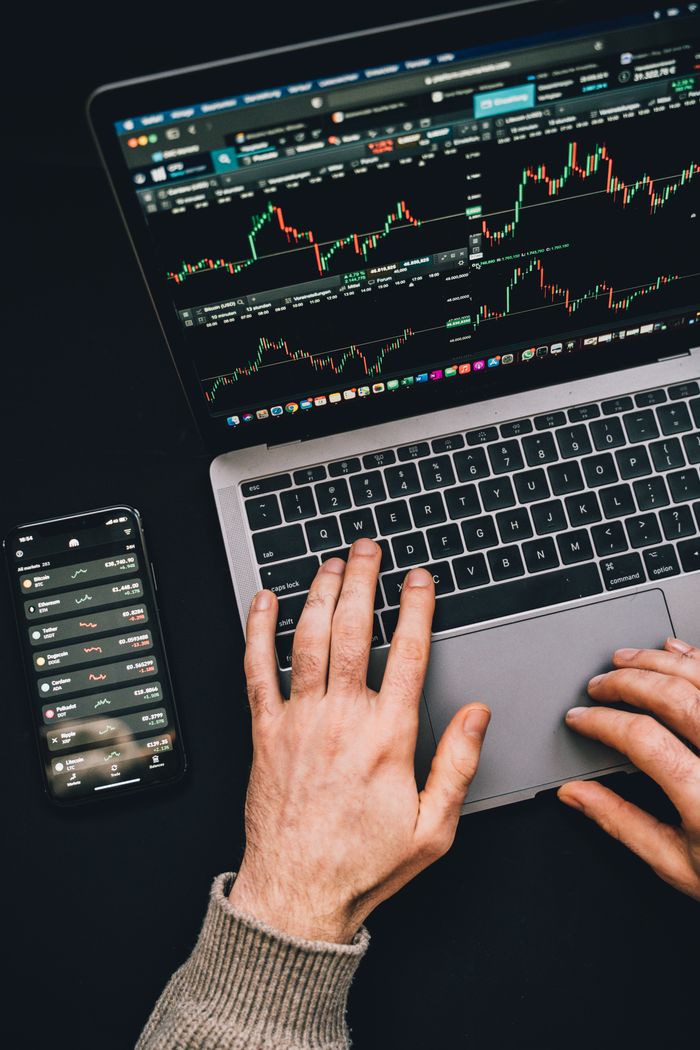 Hands at work on a laptop, with cryptocurrency charts and a smartphone visible, emphasizing digital finance.